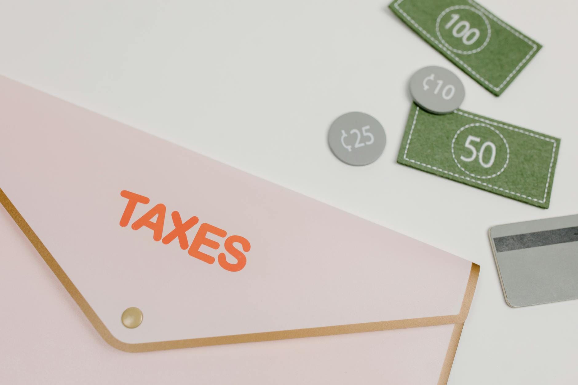 Optymalizacja podatkowo‑kosztowa a bezpieczeństwo prawne: gdzie jest granica Różowa koperta z napisem TAXES i zabawkowymi pieniędzmi na białym tle